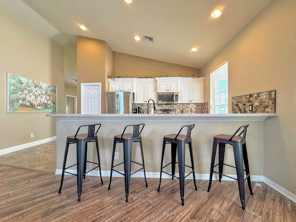 A kitchen with a central island, bar stools, and a microwave.