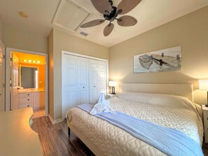 A hotel room with a bed, bedside lamps, a ceiling fan, a wardrobe, and a bathroom with a vanity and mirror.