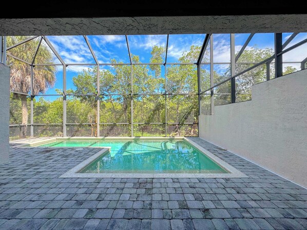 A swimming pool with a clear view of trees and sky through a glass enclosure.