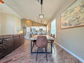 A dining area with a wooden table and chairs, a brown leather couch, and a kitchen in the background.