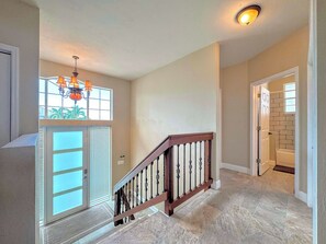 A spacious hallway with a wooden staircase, a glass door, and a ceiling light fixture.