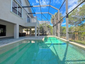 A swimming pool with a clear blue water, surrounded by a covered patio area with outdoor furniture.