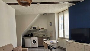 Kompakti oleskelutila, jossa on sohva, ruokapöytä, televisio ja pieni keittiö.