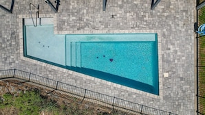 Una piscina rectangular amb un marc de rajoles, una escala metàl·lica i una petita font.