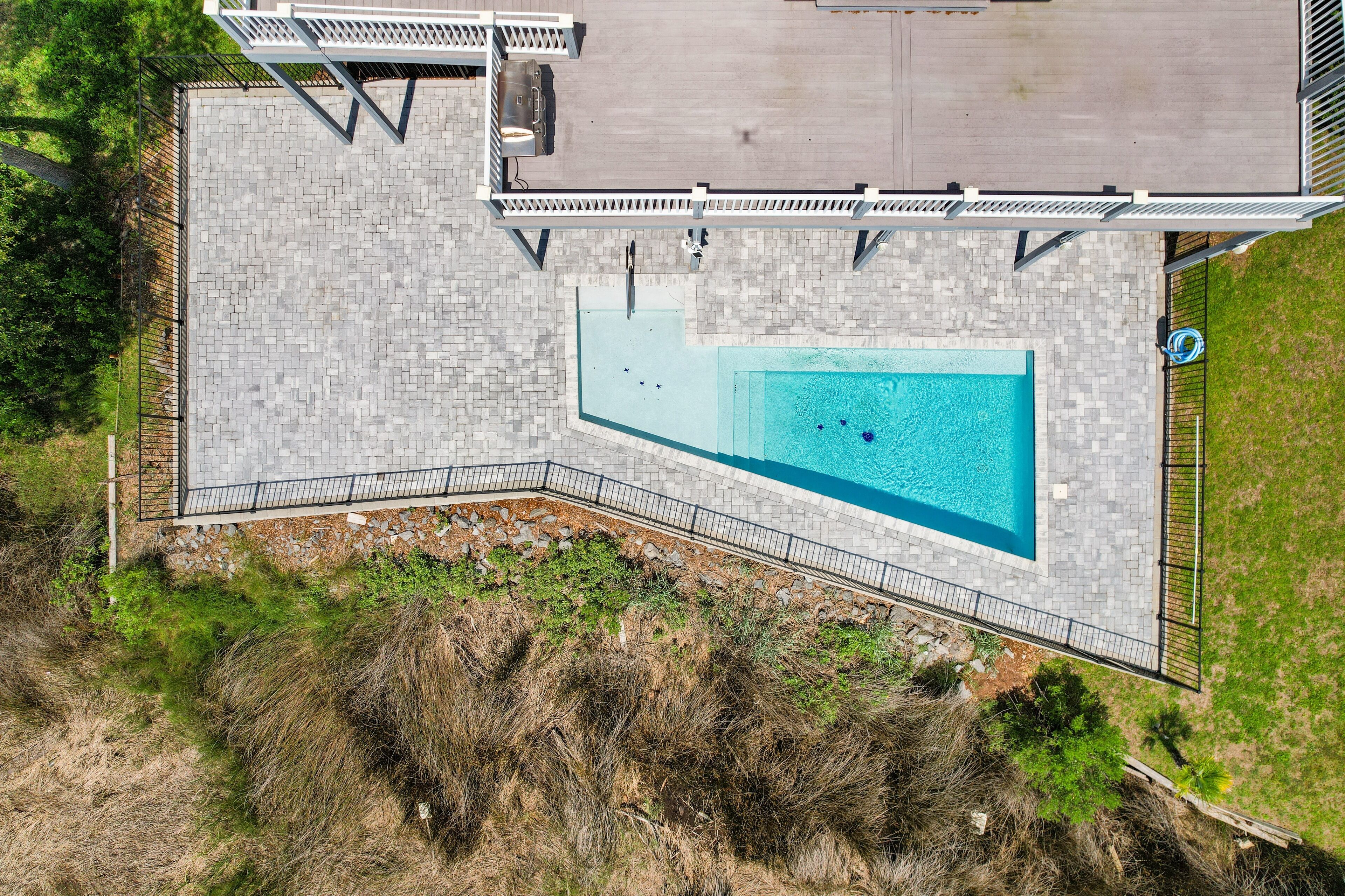 Vue aérienne d’un espace piscine comprenant une terrasse en pierre, une petite terrasse avec un barbecue et une zone herbeuse.