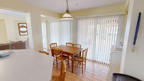 A dining area with a wooden table and chairs, a hanging light fixture, and a window with blinds. - Canal Breeze Cottage 4 Bedroom Home (Destin)