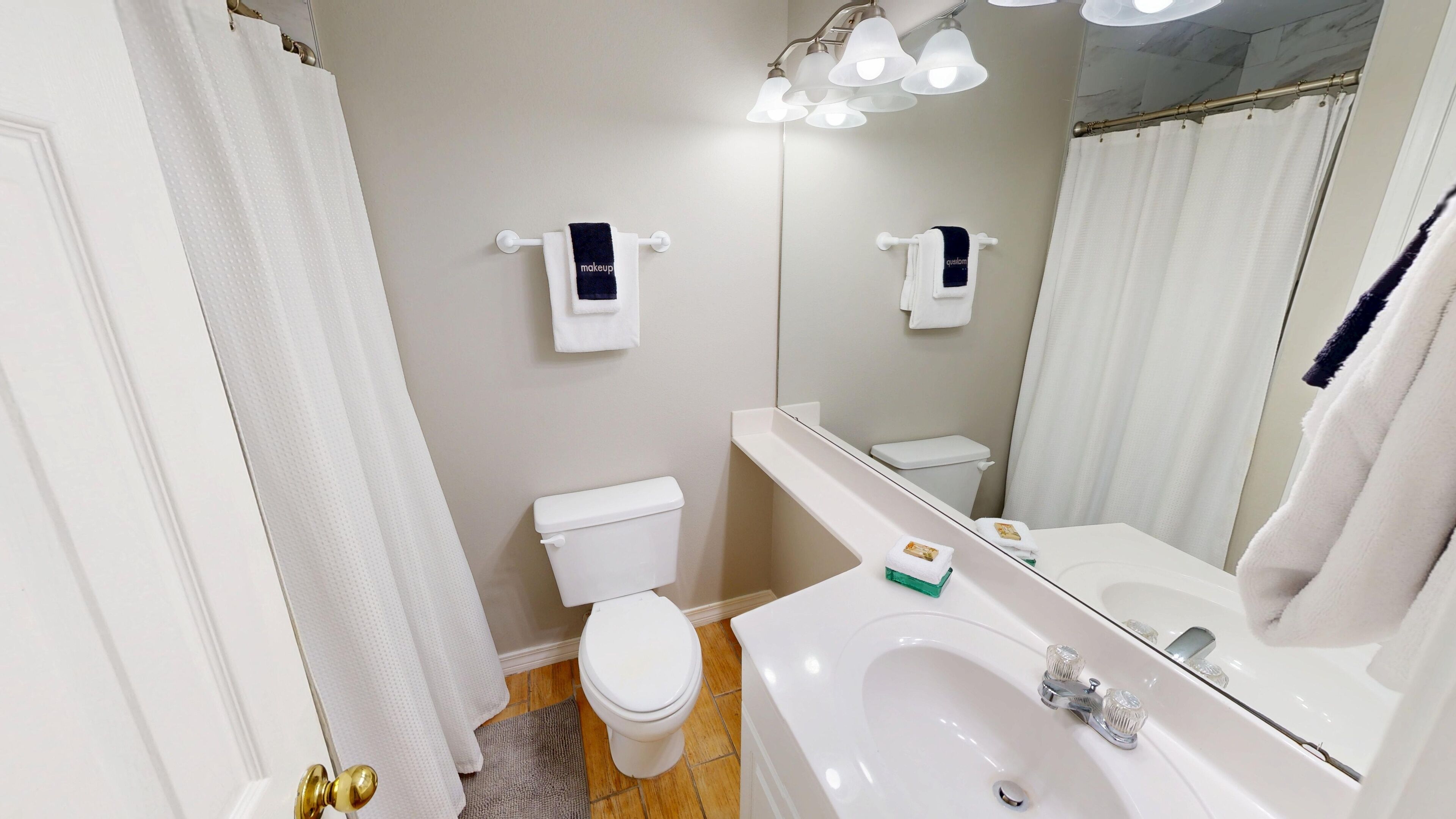 A bathroom with a toilet, sink, and mirror. There are two towel dispensers on the wall.