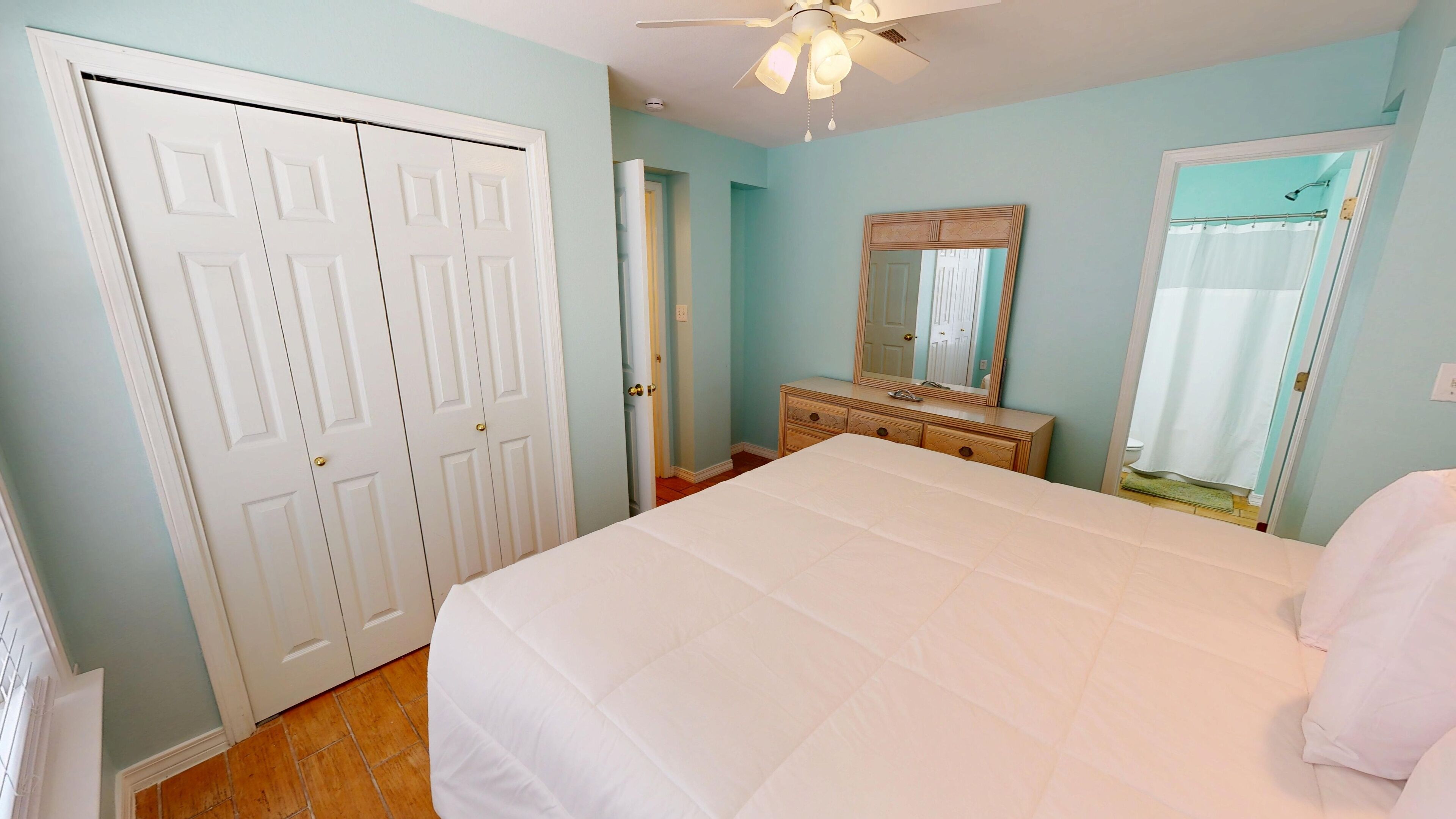 A bedroom with a large bed, a dresser, a mirror, and a ceiling fan.
