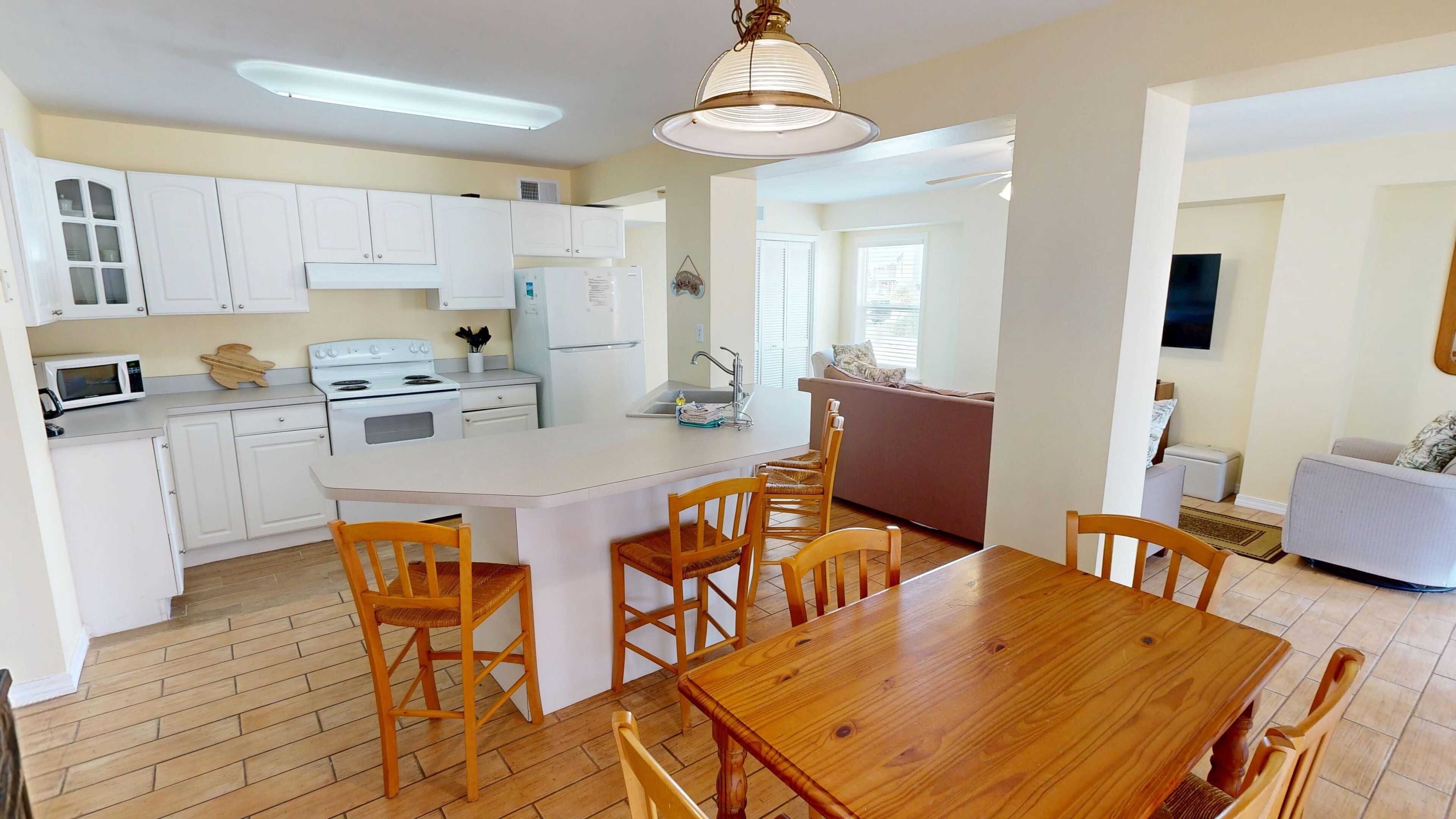 A compact kitchen with white cabinets, a central island with chairs, a microwave, and a stove.