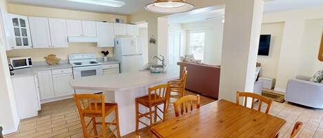 A compact kitchen with white cabinets, a central island with chairs, a microwave, and a stove.