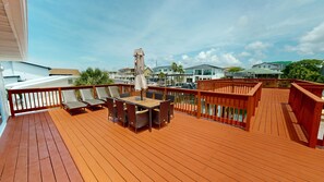 A wooden deck with a table and chairs, a red railing, and a view of houses across a body of water. - Canal Breeze Cottage 4 Bedroom Home (Destin)