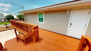 A residential building with a wooden deck, a garage door, and a window with a green screen. - Canal Breeze Cottage 4 Bedroom Home (Destin)