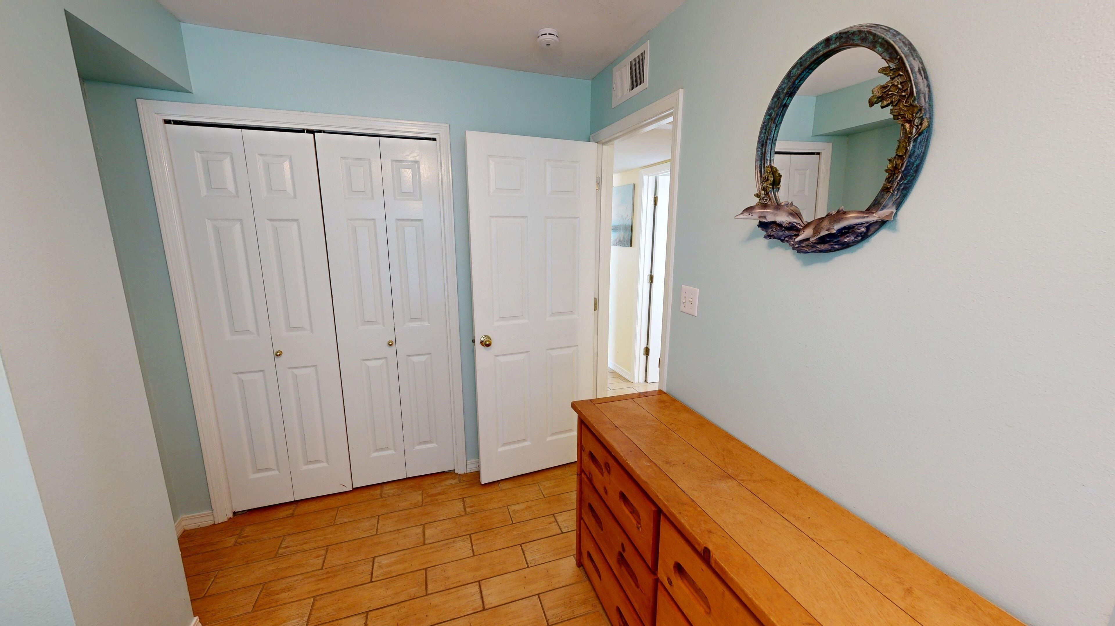 A hallway with a wooden dresser, a mirror with a decorative frame, and a set of white double doors.