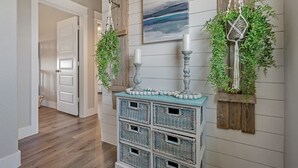 A hallway with a wooden floor, a white door, a wall-mounted wicker basket unit, and two wall-mounted macramé planters with greenery. - B3 Sand Ranch 4 Bedroom Home (Port Bolivar)