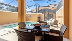 A covered outdoor area with a pool, wicker furniture, and a glass table. - Sunny Paradise Retreat At Paradise Palms By Shine Villas 4 Bedroom Townhouse (Kissimmee)