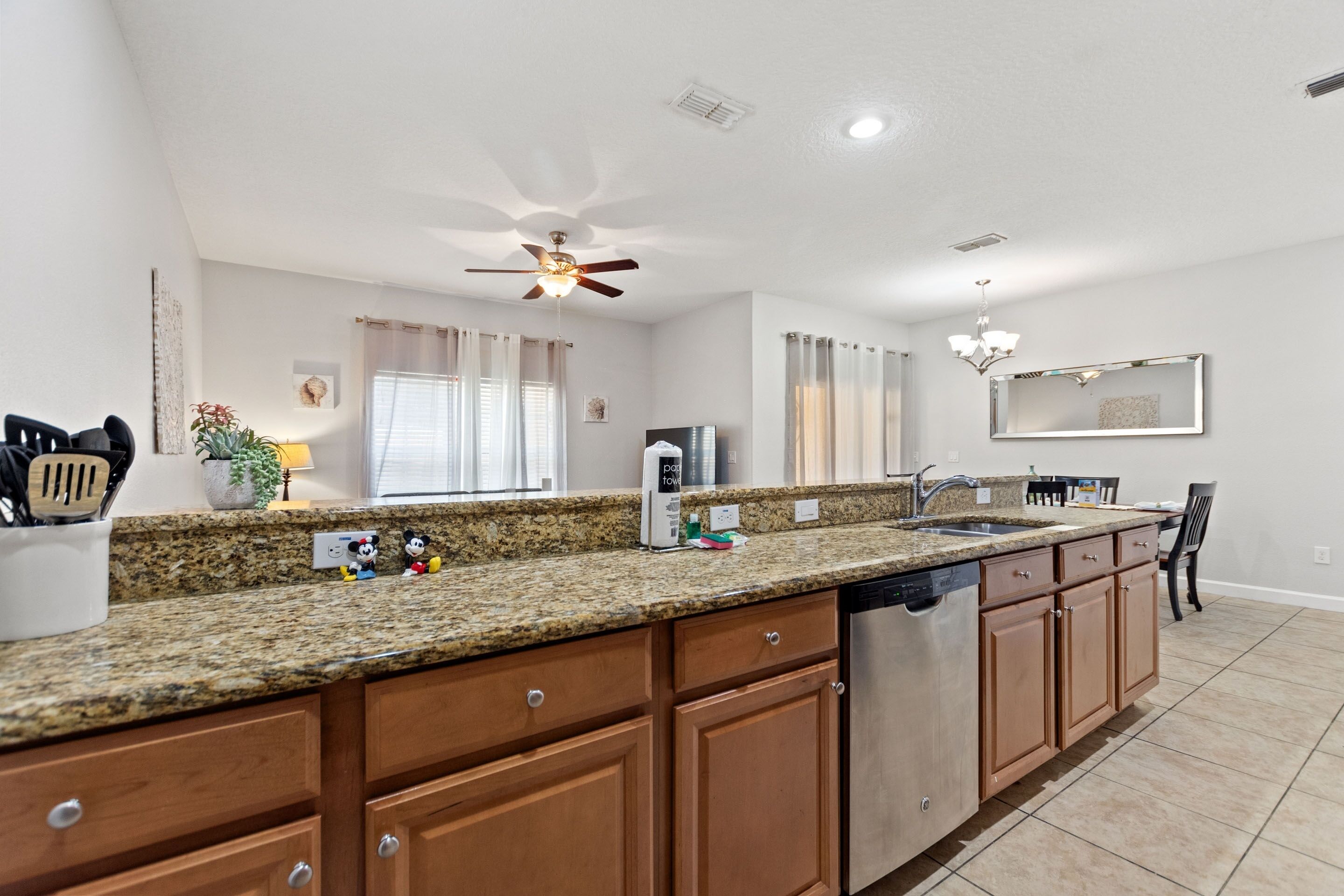 A modern kitchen with granite countertops, wooden cabinets, a dishwasher, and a ceiling fan.