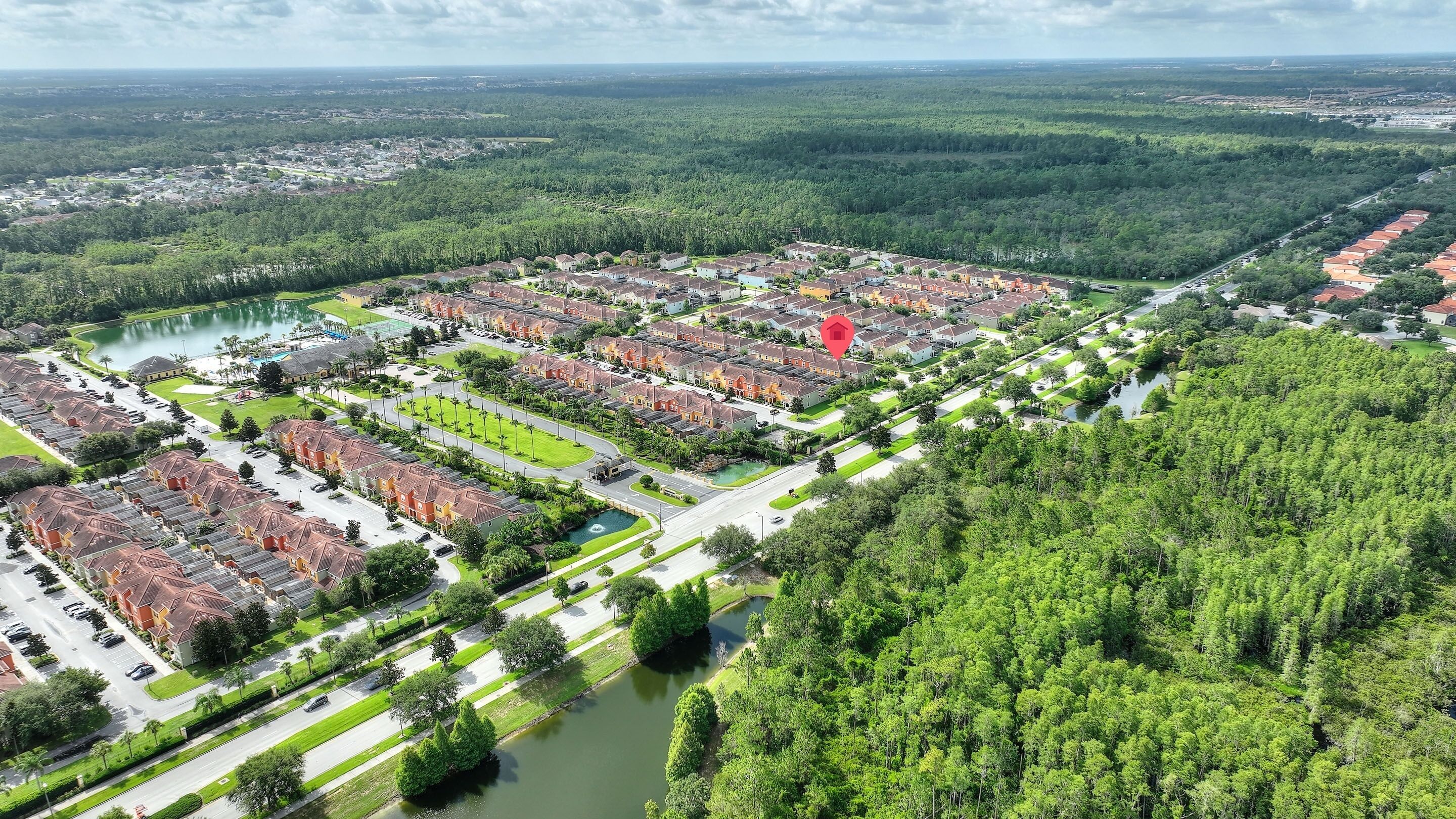 Luchtbeeld van een woongebied met meerdere rijen huizen, een centrale weg en een waterpartij.