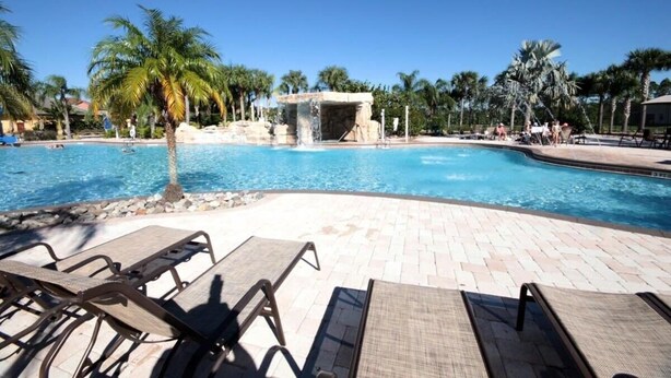A pool area with lounge chairs, palm trees, and a water feature. - Sunny Paradise Retreat At Paradise Palms By Shine Villas 4 Bedroom Townhouse (Kissimmee)
