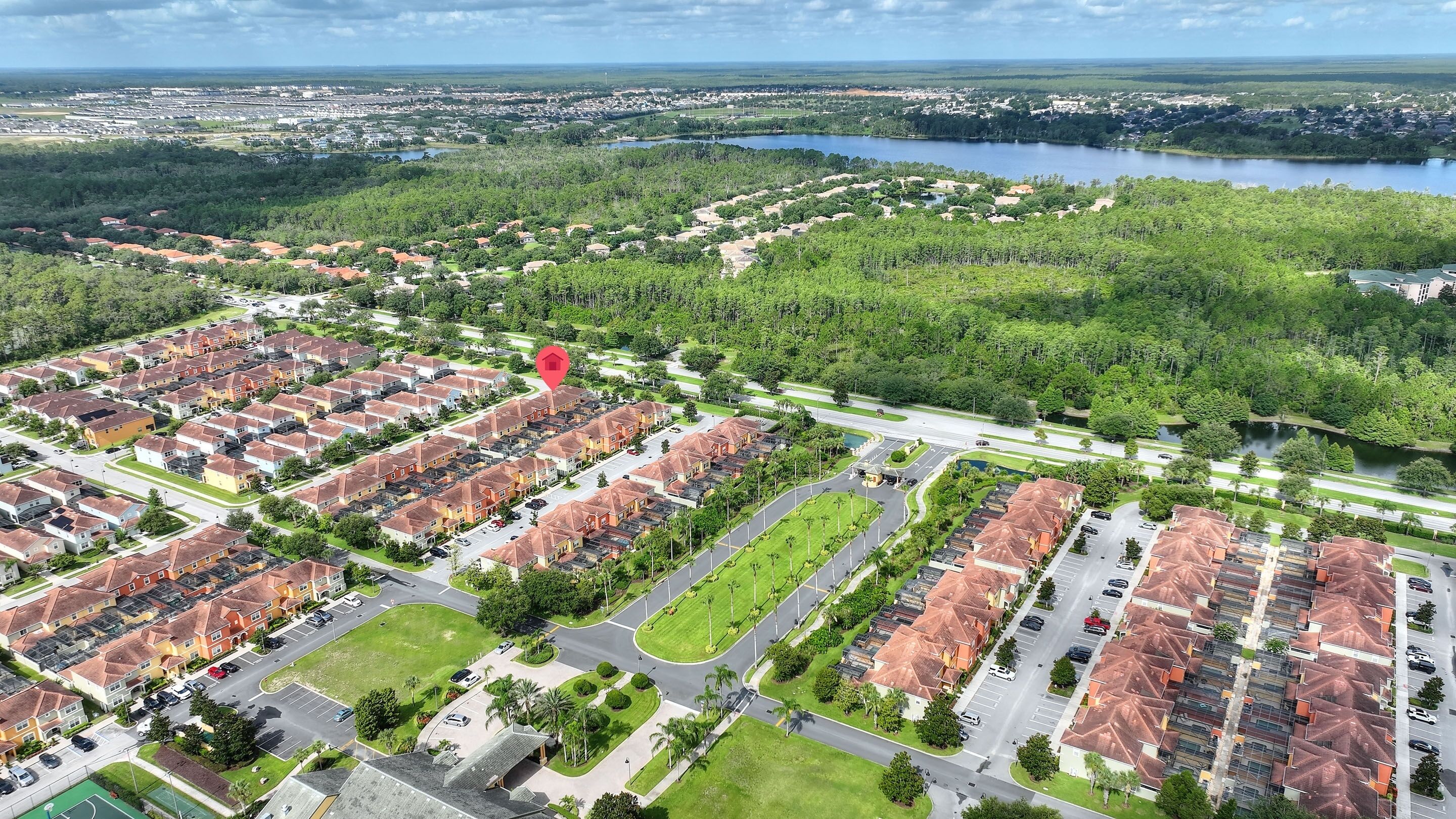 Un barrio residencial con varias filas de casas, una avenida central y un lago al fondo.