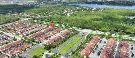 Un barrio residencial con varias filas de casas, una avenida central y un lago al fondo.