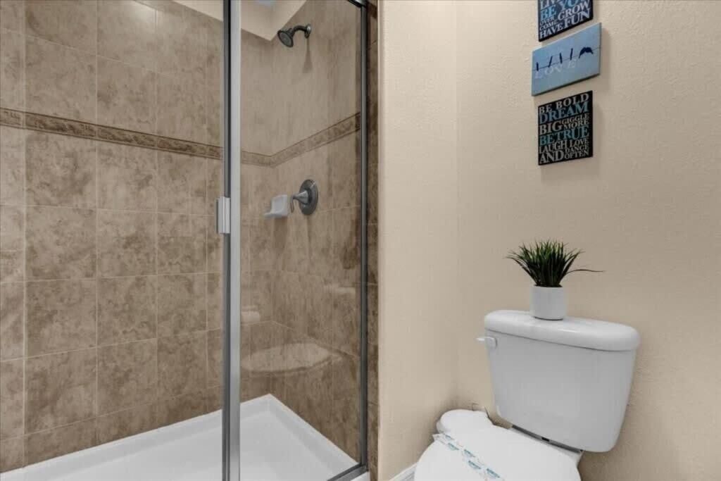 Une salle de bain avec une douche à parois de verre, des toilettes blanches et une petite plante en pot posée sur le réservoir des toilettes.