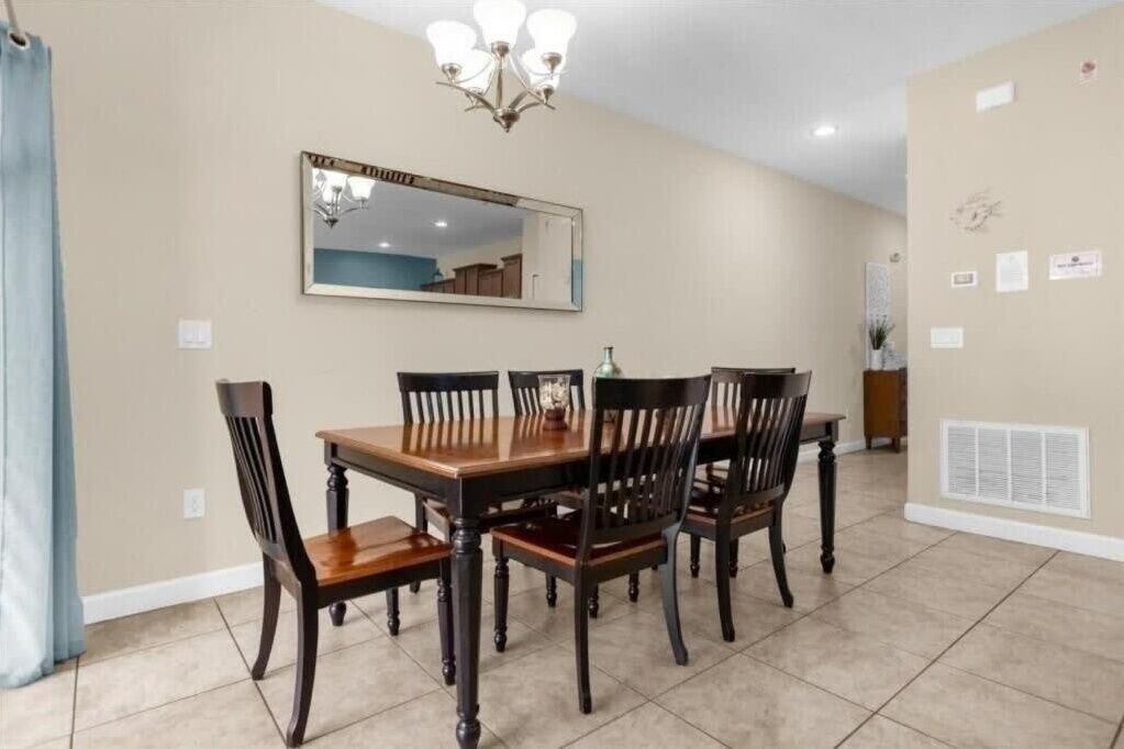 A dining area with a wooden table and chairs, a chandelier, a mirror, and a wall with framed certificates.