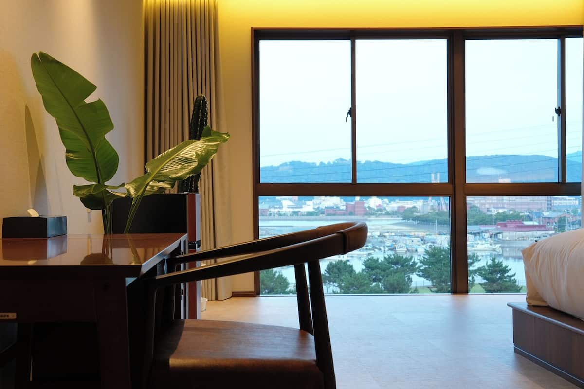 A hotel room with a large window offering a view of a cityscape and water.