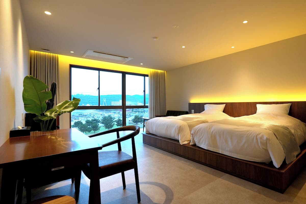 A hotel room with a large bed, a desk, and a view of a bridge and cityscape.