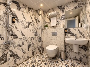 A bathroom with a shower, toilet, sink, and marble-patterned walls. - Livane Beach Otel (Alanya)