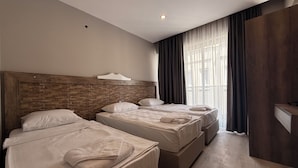 Een hotelkamer met twee bedden, een houten hoofdbord, een nachtkastje en een groot raam met gordijnen.
