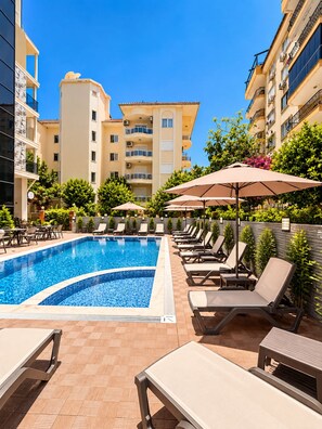 A swimming pool with lounge chairs and umbrellas, surrounded by buildings. - Livane Beach Otel (Alanya)