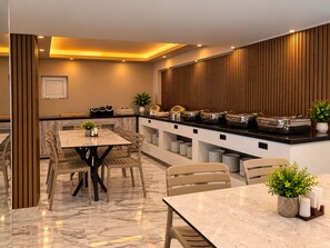 A modern dining area with a marble floor, wooden paneling on the walls, and a buffet setup with various food containers. - Livane Beach Otel (Alanya)