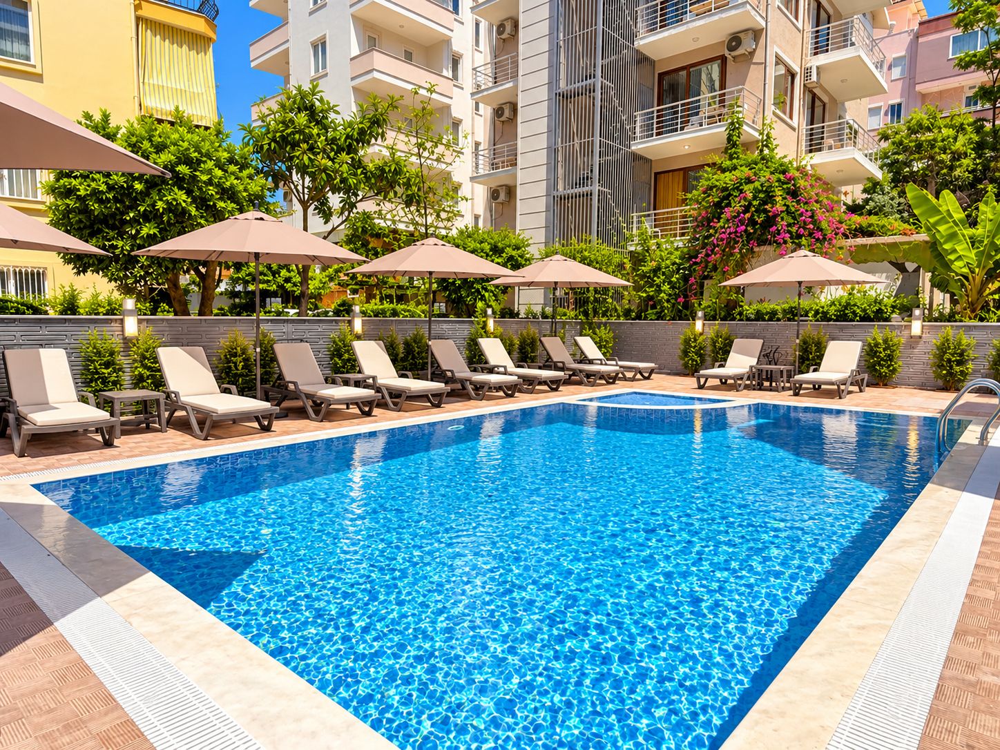 Piscina con sillas de descanso y sombrillas, rodeada por un edificio de varios pisos con balcones.