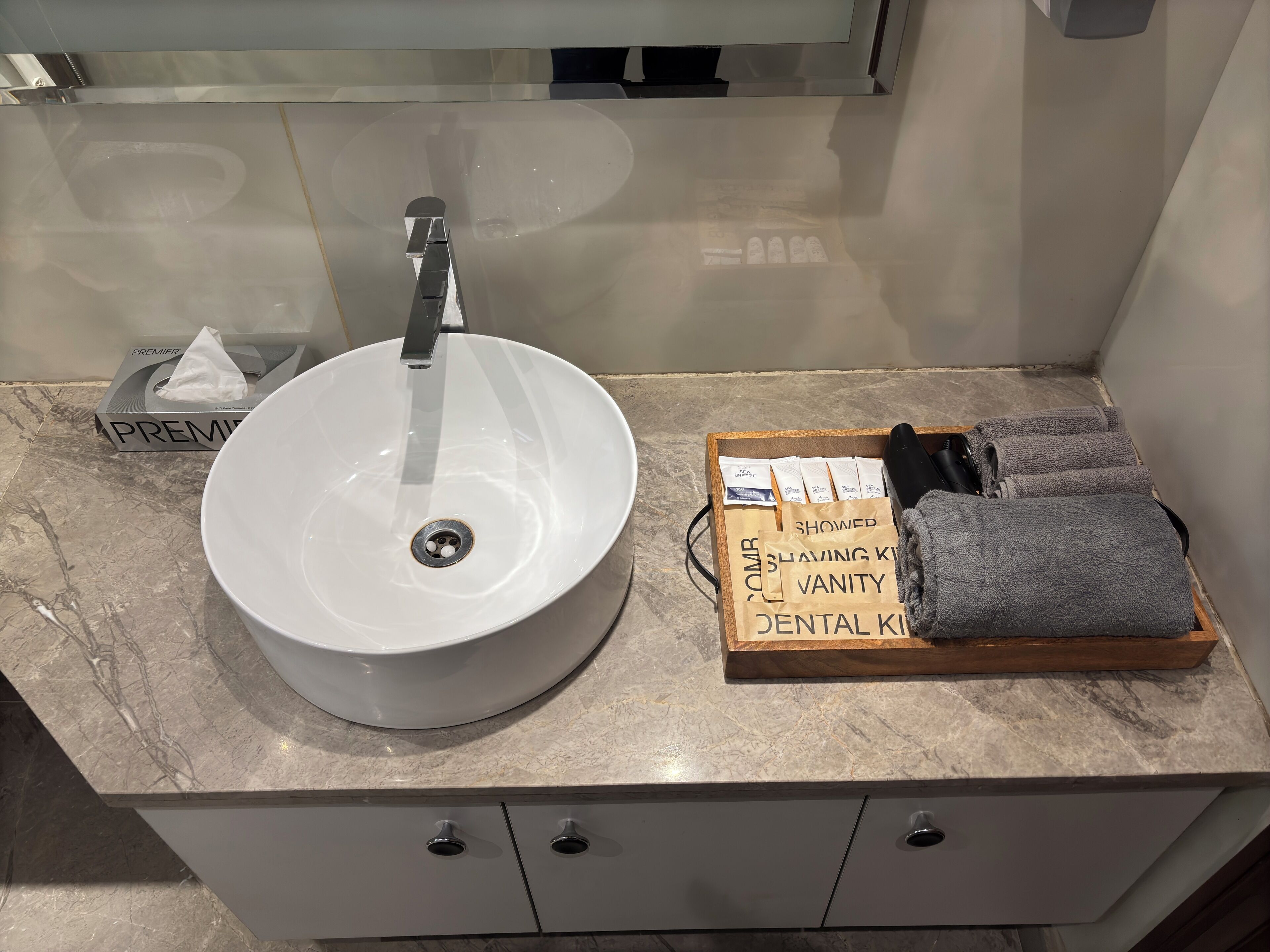 A bathroom with a white sink, a tissue box, and a tray with towels and shaving kits.