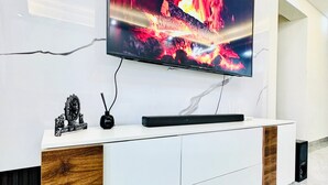 Un salon moderne doté d’un grand téléviseur à écran plat fixé au mur, d’une console blanche agrémentée de détails en bois et d’une sculpture décorative.