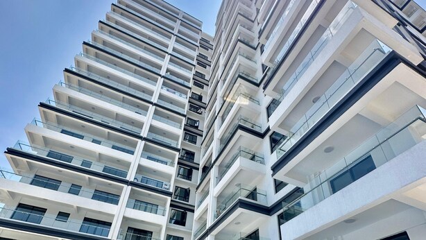 Un immeuble résidentiel de grande hauteur doté de nombreux balcons, d’un espace piscine et offrant une vue sur un ciel dégagé.