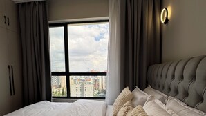 Une chambre d’hôtel avec deux lits, une grande fenêtre avec des rideaux, une vue sur la ville et un luminaire fixé au mur.