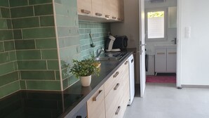 A kitchen with green tiled backsplash, a potted plant on the counter, and a view into the adjacent bathroom.