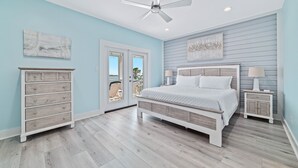 A bedroom with a bed, dresser, nightstand, ceiling fan, and artwork on the walls.
