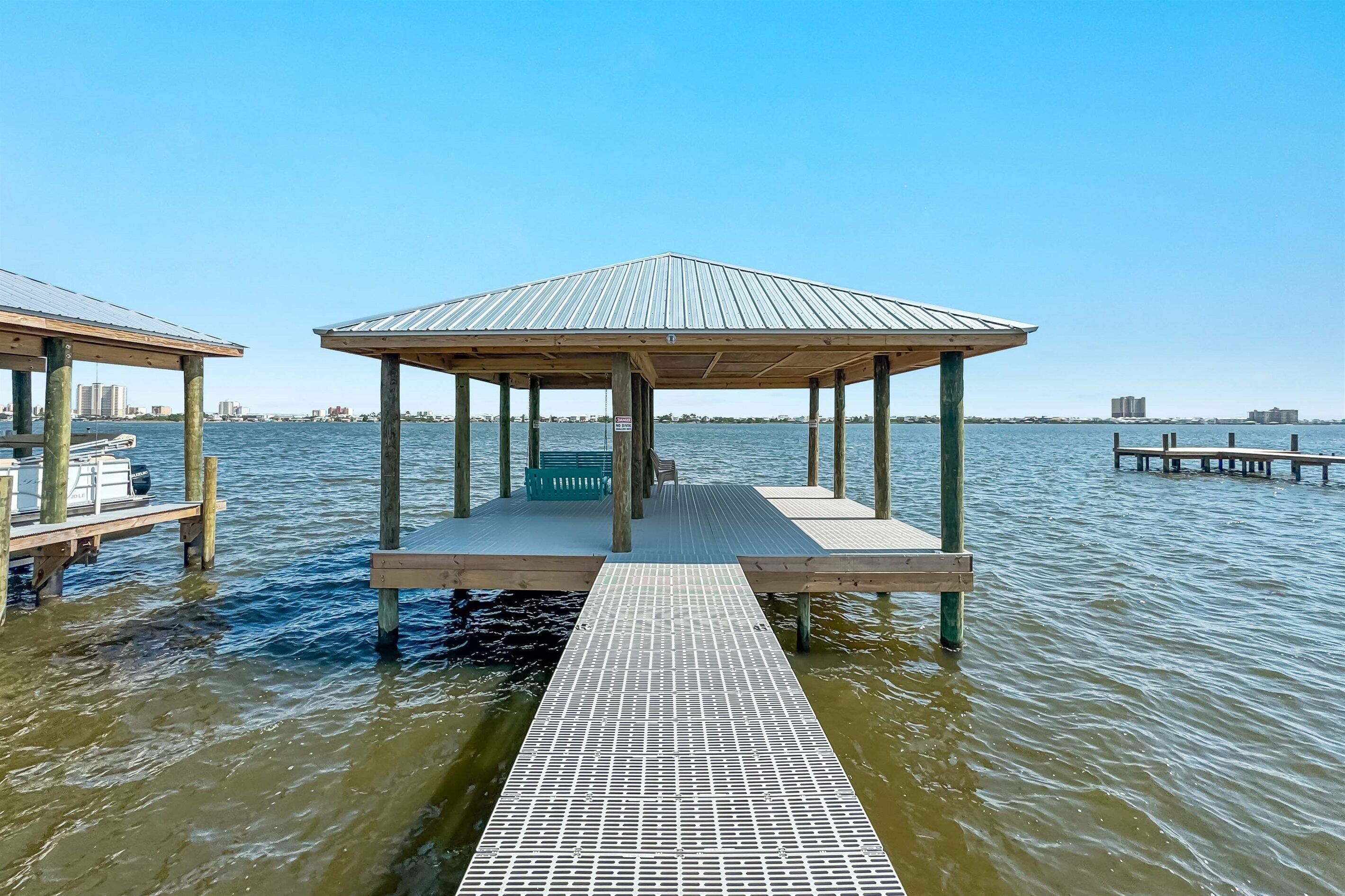 A wooden pier with a covered seating area and a metal walkway leading to it.