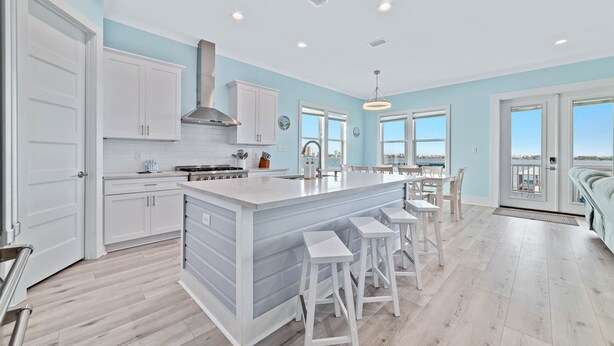 A modern kitchen with white cabinets, a large island with bar stools, and a view through the windows.