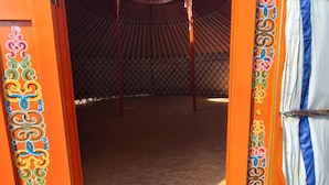 Una tienda de campaña con una entrada abierta, una estructura circular de madera en su interior y un diseño estampado en la puerta.