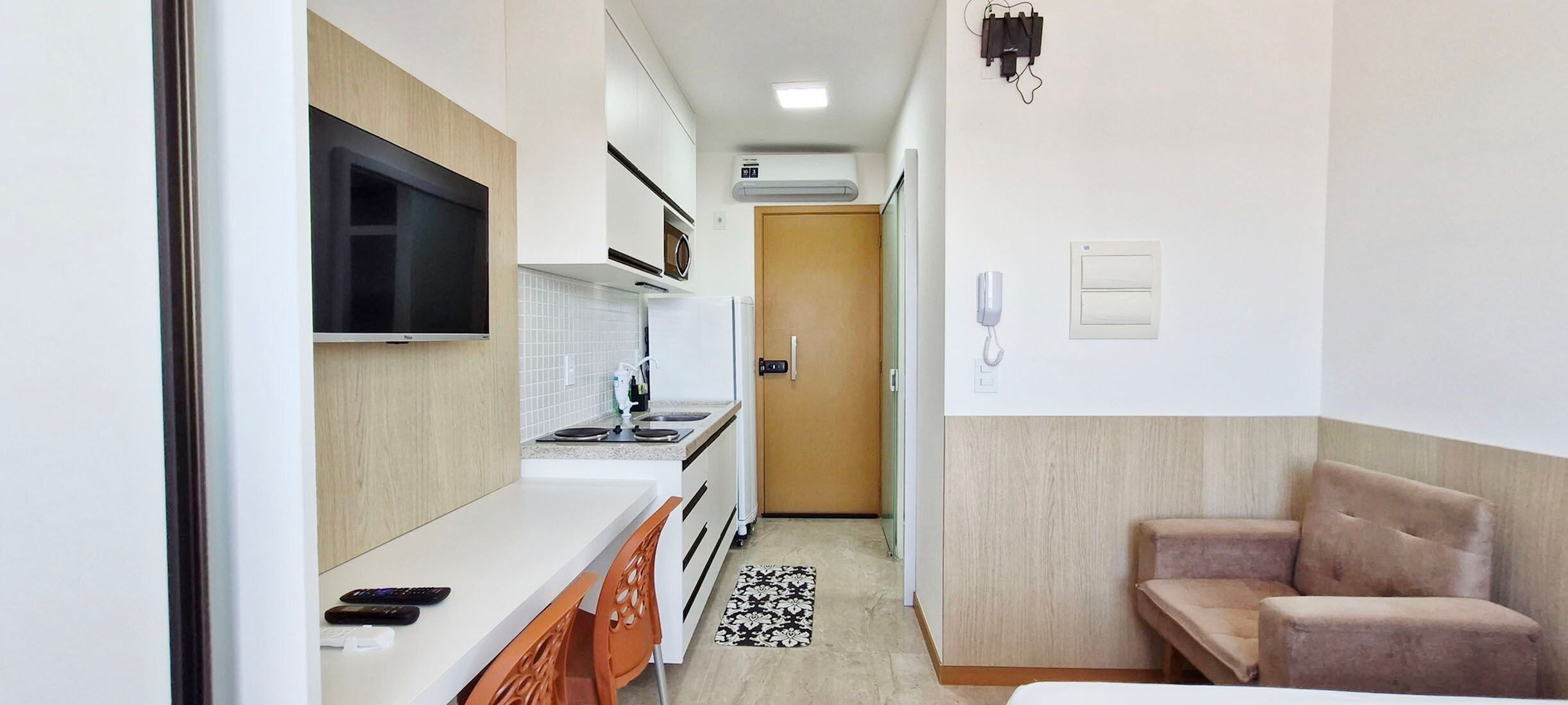 A compact kitchen with a microwave, stove, and a TV mounted above the counter.