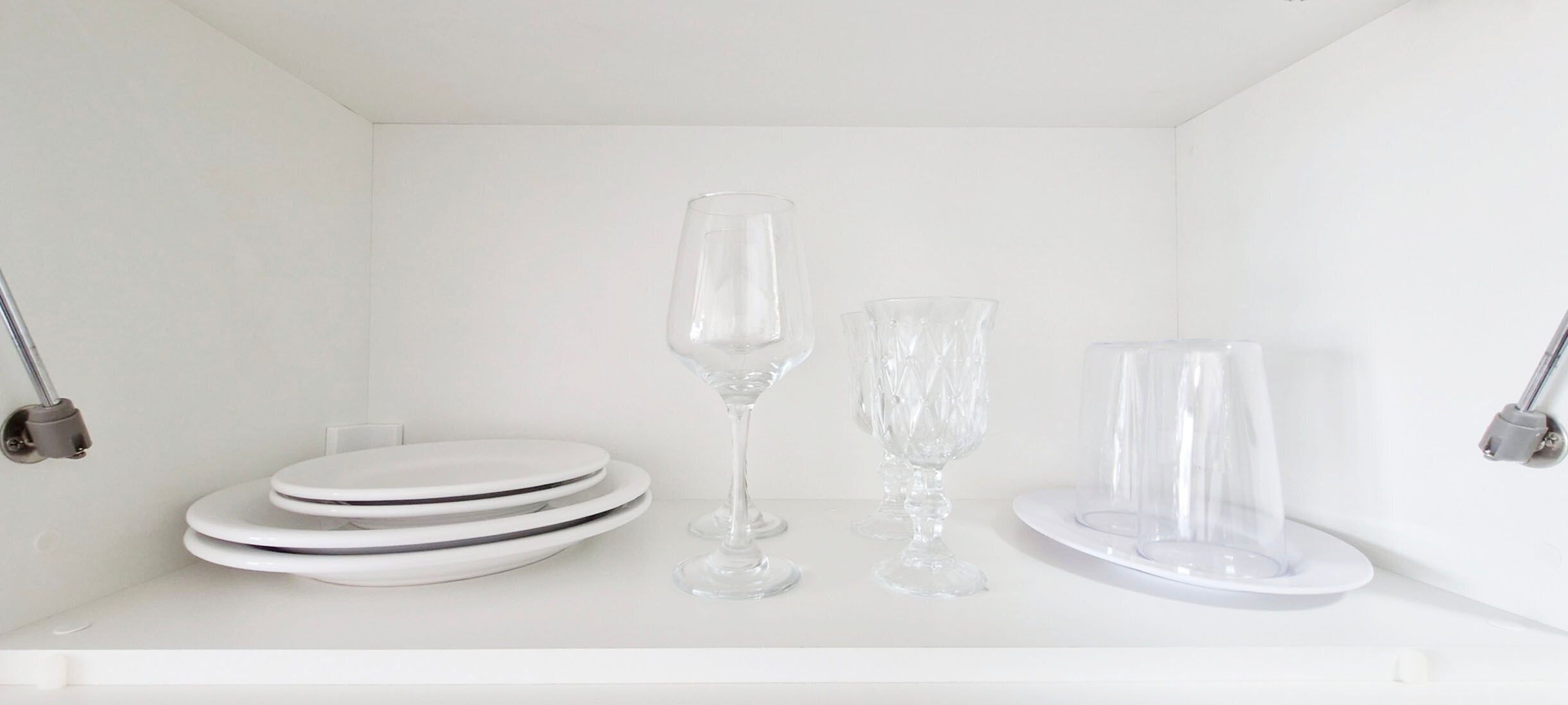 Une étagère blanche sur laquelle sont empilées des assiettes, ainsi que trois objets en verre transparent.