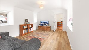 Un salón espacioso con un sofá gris, estanterías de madera, un televisor de pantalla plana y una alfombra con rayas coloridas.