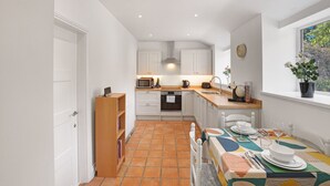 Una cocina compacta con armarios blancos, un microondas y un lavamanos. Hay una mesa de comedor preparada con platos y vasos.
