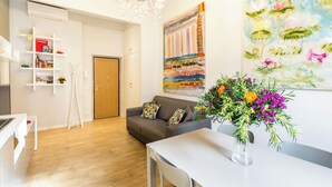A modern living room with a wooden floor, a grey sofa, a white table, and a colorful painting on the wall.