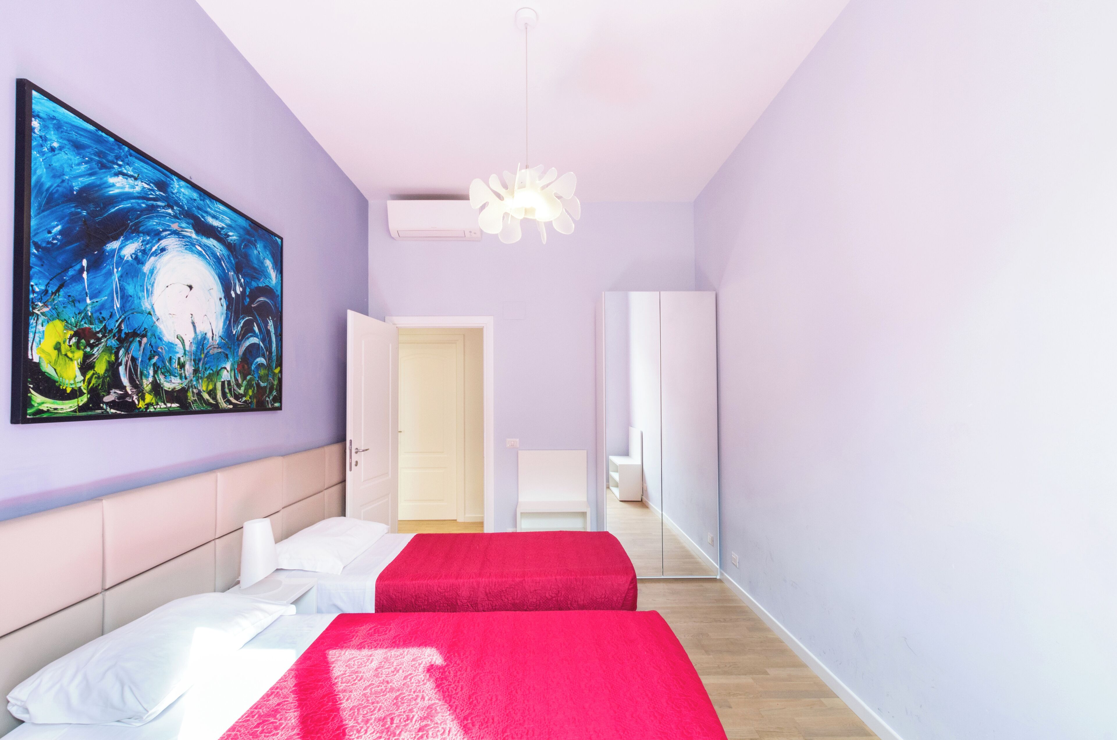 Una habitación de hotel con una cama, un cuadro, una silla blanca y una puerta.