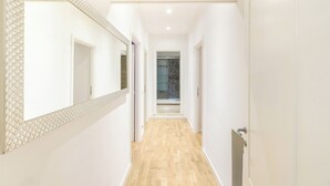 A hallway with a wooden floor, white walls, and a large mirror on the left.