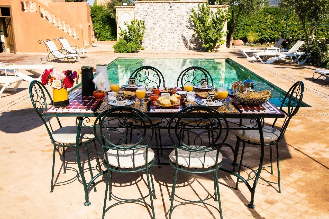 An outdoor dining area with a pool, surrounded by lounge chairs and a stone wall.